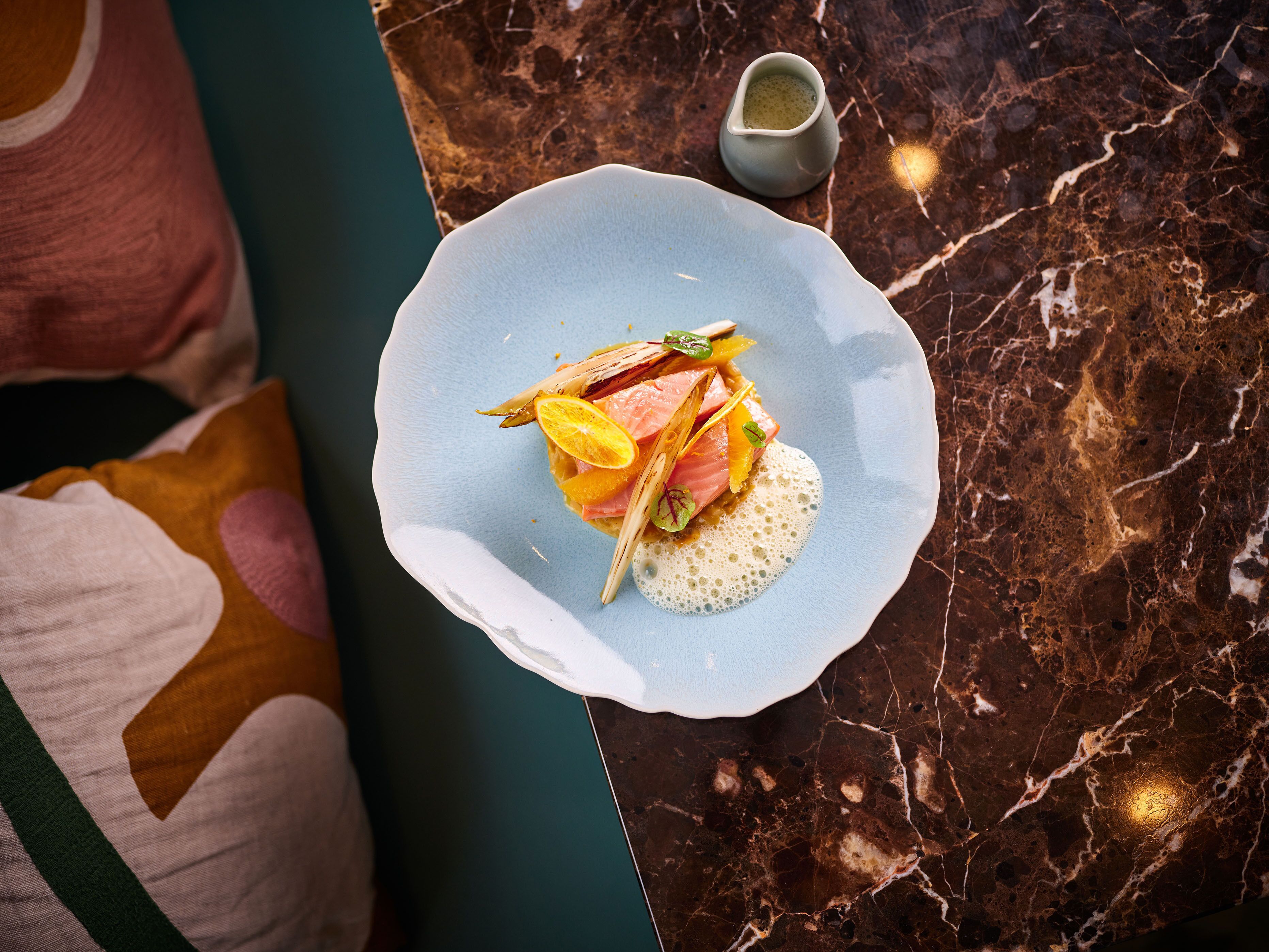 A plate of food on a marble table with a small pitcher of sauce.