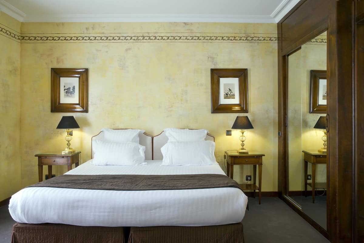 A neatly made bed with white linens, two bedside tables with lamps, and framed pictures on the walls.