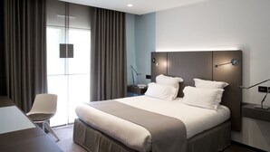 Una habitació d'hotel moderna amb un llit gran, una taula de treball i una cadira.