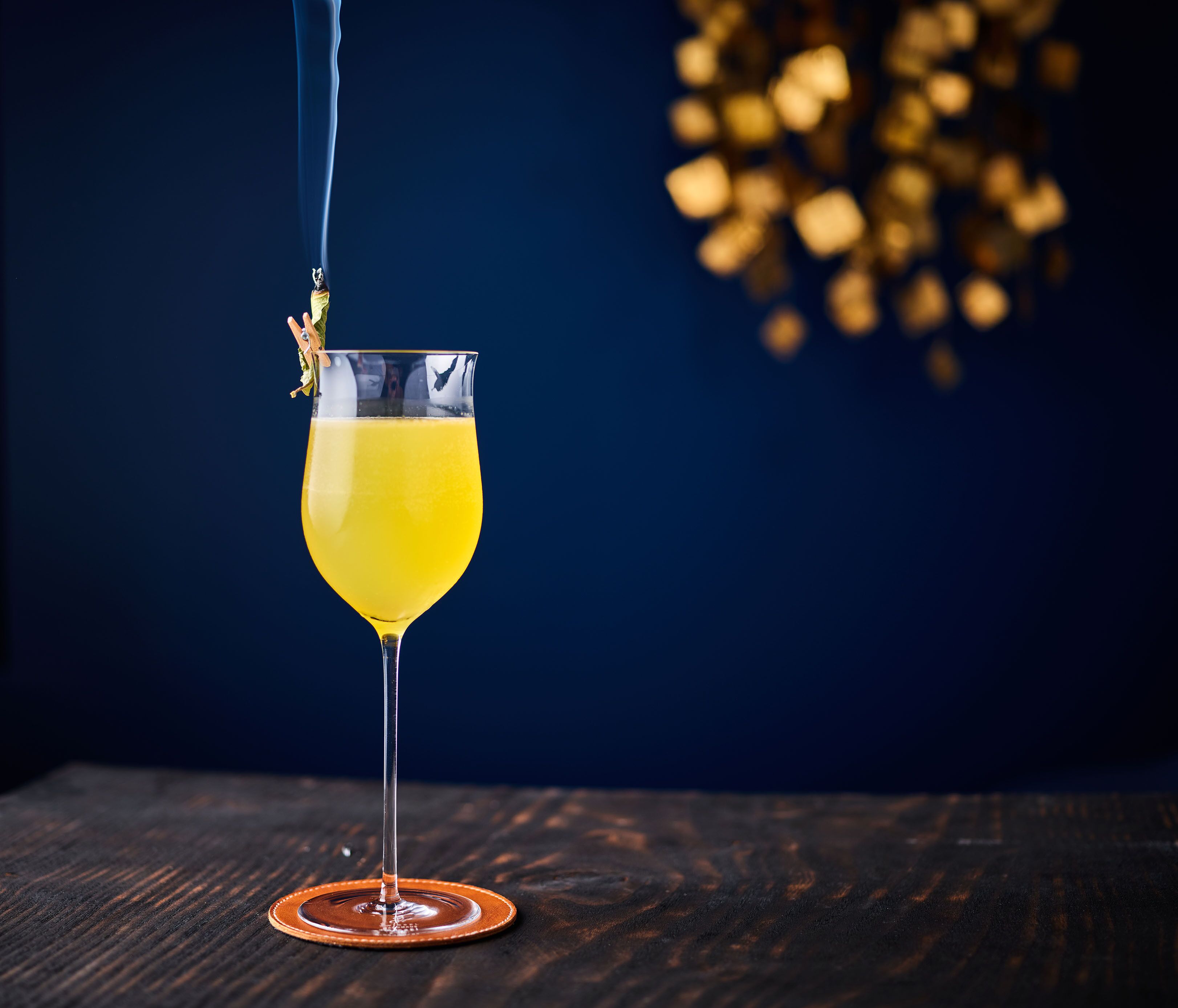 A cocktail glass with a yellow liquid on a wooden surface.