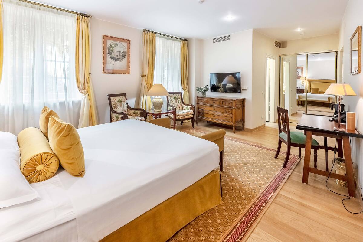 A hotel room with a large bed, a desk, a chair, a television, and a wardrobe.