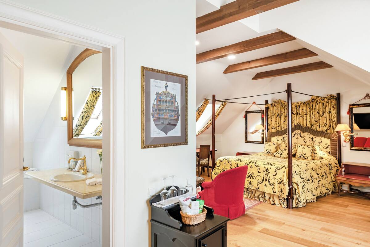 A bedroom with a four-poster bed, a large mirror, a framed picture, and a small table with a basket.