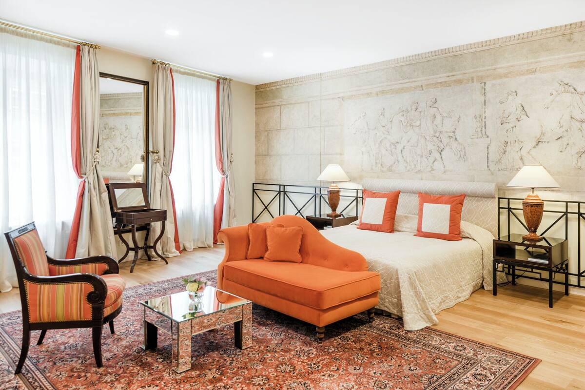 A hotel room with a bed, orange sofa, armchair, and a small table.