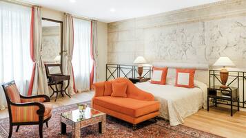 Una habitación de hotel con cama, sofá naranja, sillón y una mesita.
