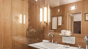 Un baño moderno con ducha envuelta en vidrio, tocador de madera con dos lavamanos y un espejo grande.