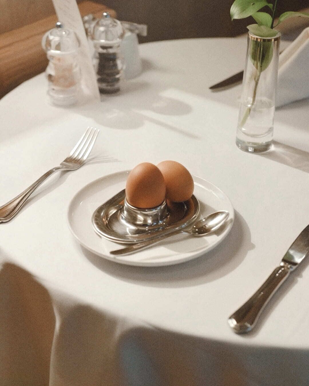 Una mesa de comedor con un plato de dos huevos, un tenedor, un cuchillo y una cuchara.