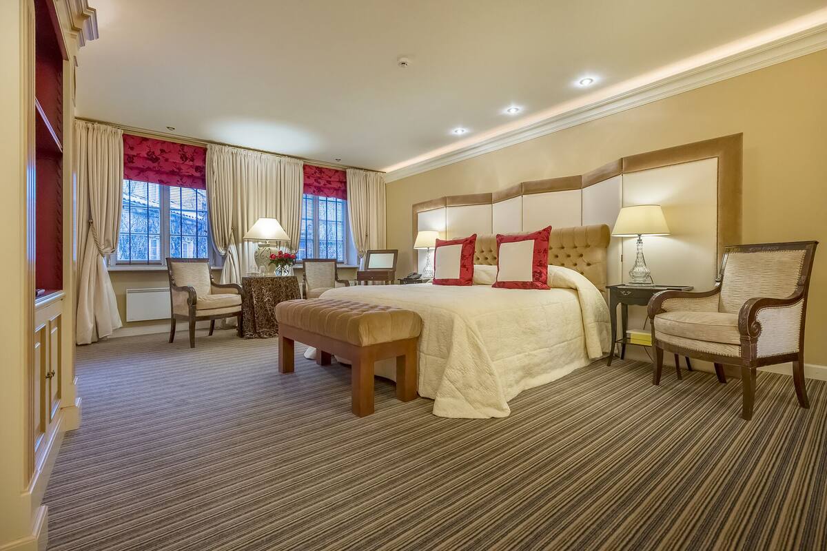 A hotel room with a large bed, two bedside tables with lamps, a chair, a desk, and a window with curtains.