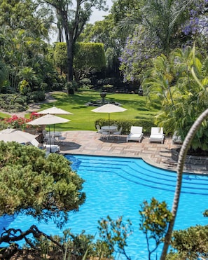A swimming pool with lounge chairs and umbrellas, surrounded by well-maintained greenery and a lawn.