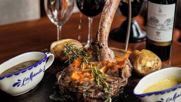 Un plato de filete con romero, acompañado de una botella de vino, una copa de vino tinto y dos salseras con salsa.