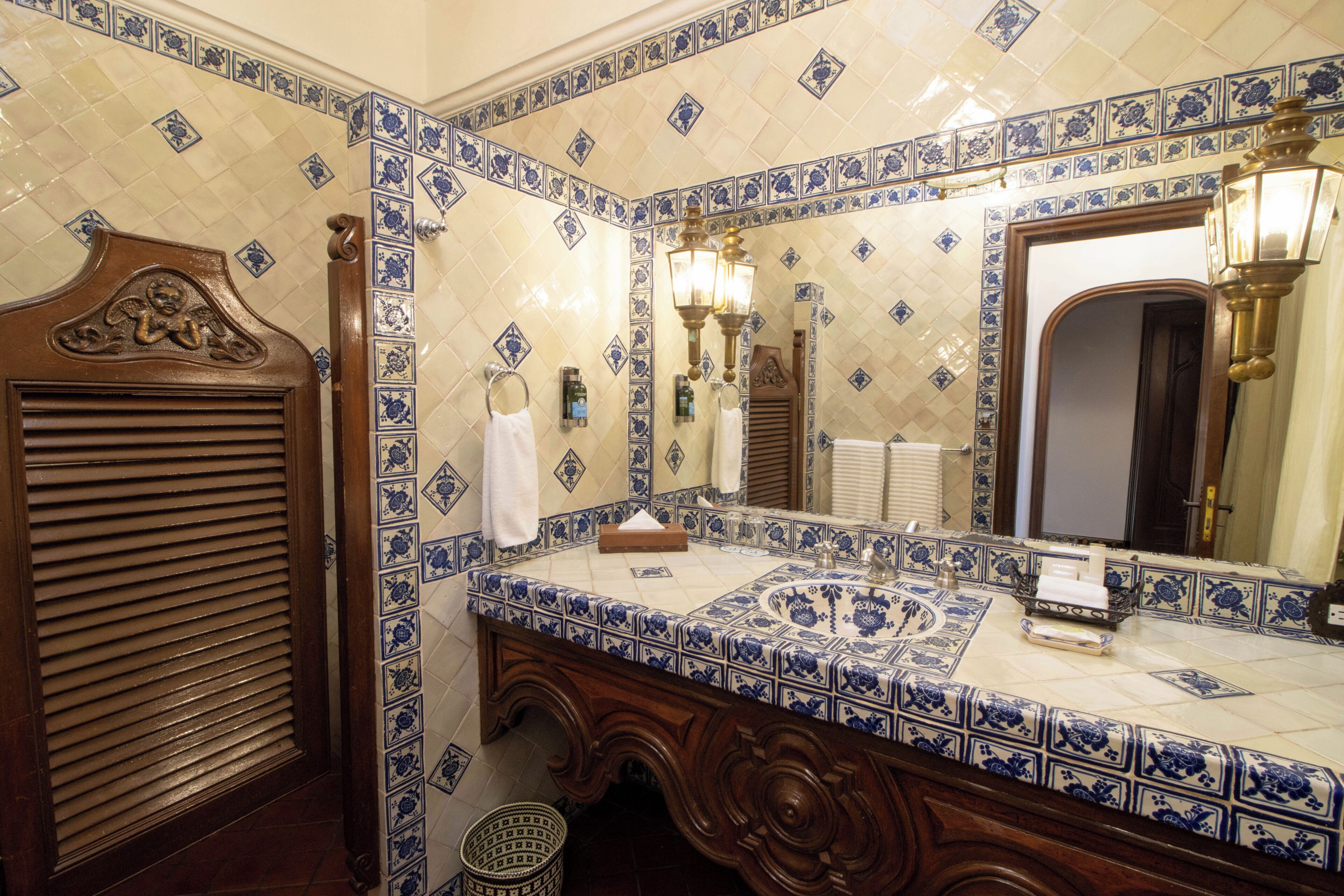 A bathroom with a tiled wall, a sink, a mirror, and a wooden door.