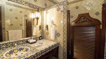 Un baño con salpicadero de azulejos estampados, un lavabo con pileta decorativa, un espejo y una puerta de madera con pomo decorativo.