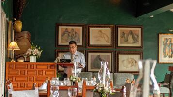 Un interior de restaurante con mesas y sillas de madera, obras de arte enmarcadas en las paredes y una persona de pie en la barra.