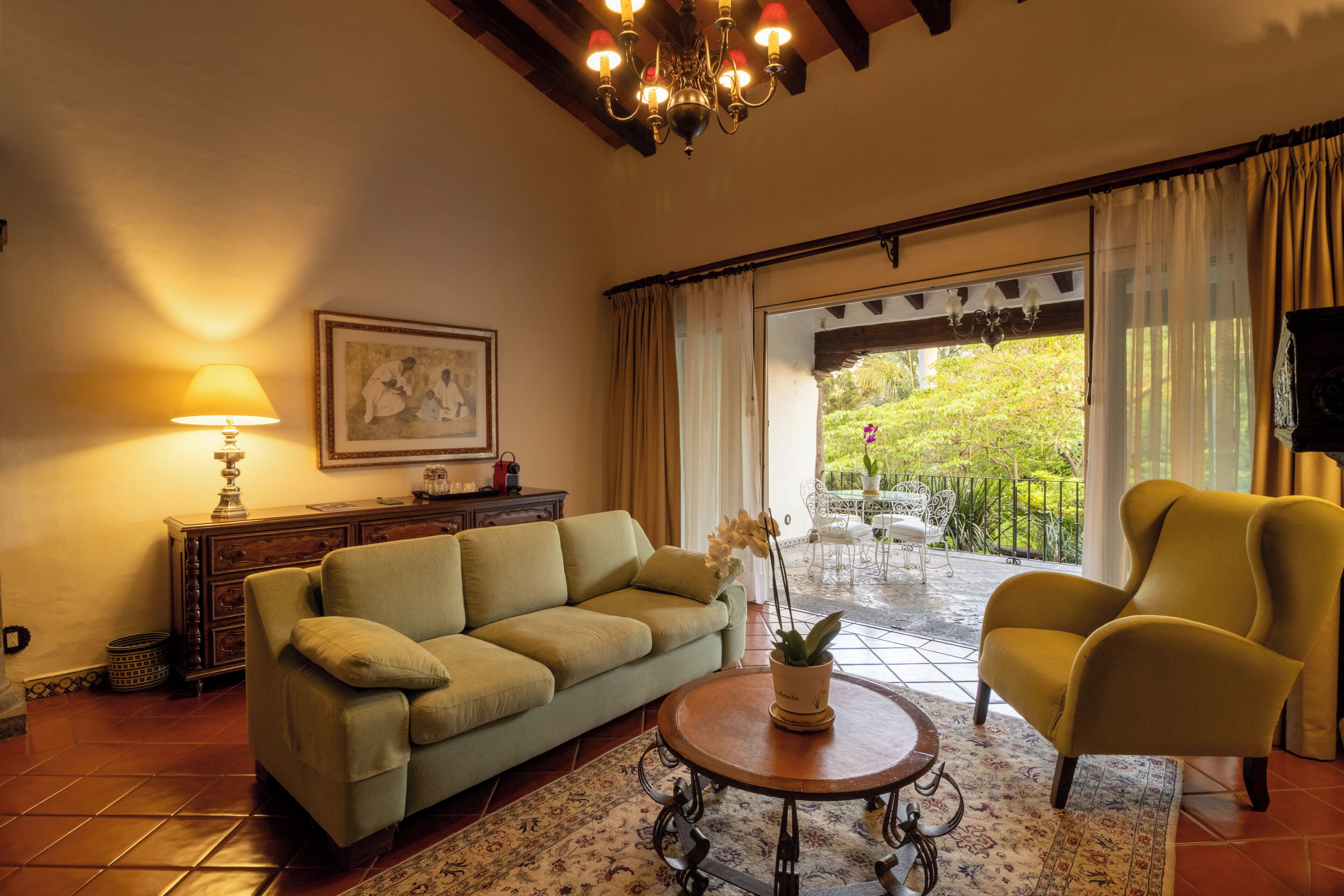 Un salón con sofá, sillón, lámpara y vistas al exterior.