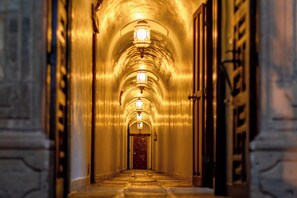 A corridor with arched ceilings and wall-mounted lights, leading to a door at the end.