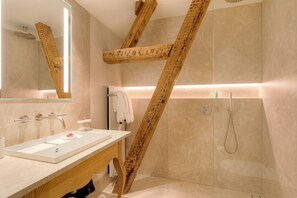 A modern bathroom with a wooden beam structure, a large mirror, a sink with a soap dish, and a shower area. - Chateau Wittem (Wittem)