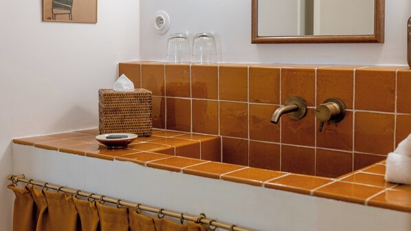 A bathroom with a tiled sink, a wicker basket, a towel rack, and a mirror.