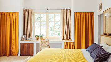 Una habitación con una cama, un escritorio con una silla, una ventana con cortinas y un armario pequeño.