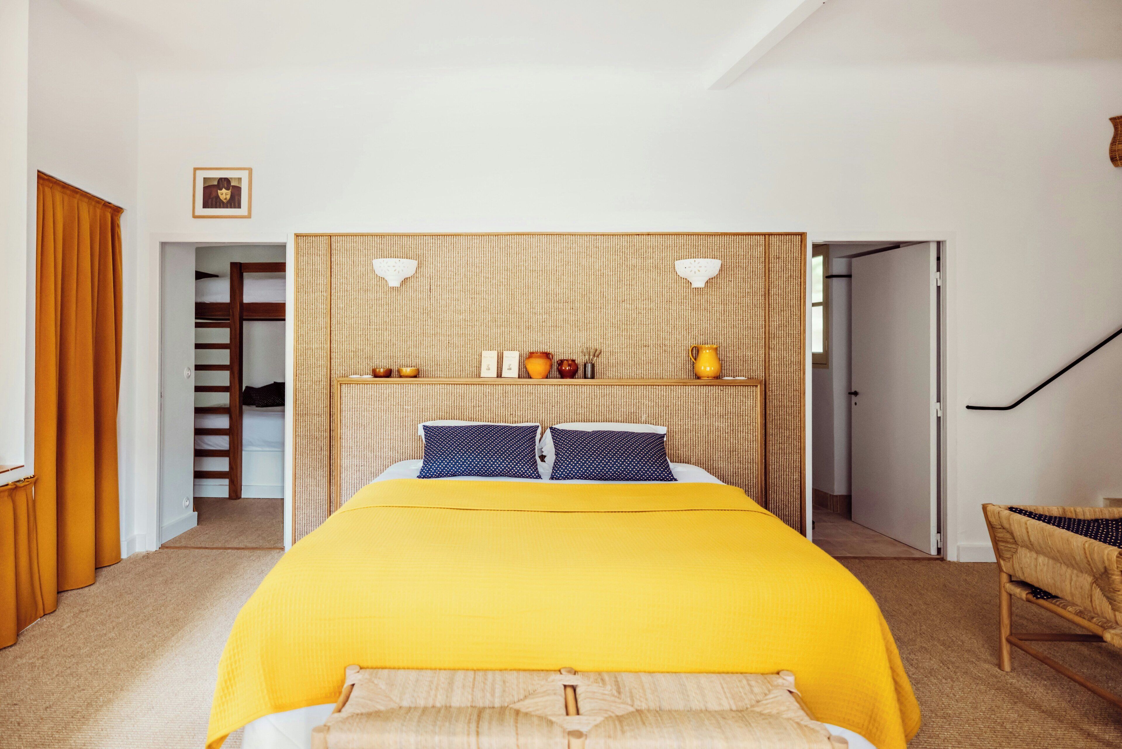 A bedroom with a bed, a headboard with shelves, a picture on the wall, and a staircase.