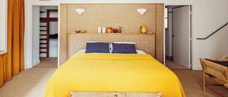 A bedroom with a bed, a headboard with shelves, a picture on the wall, and a staircase.