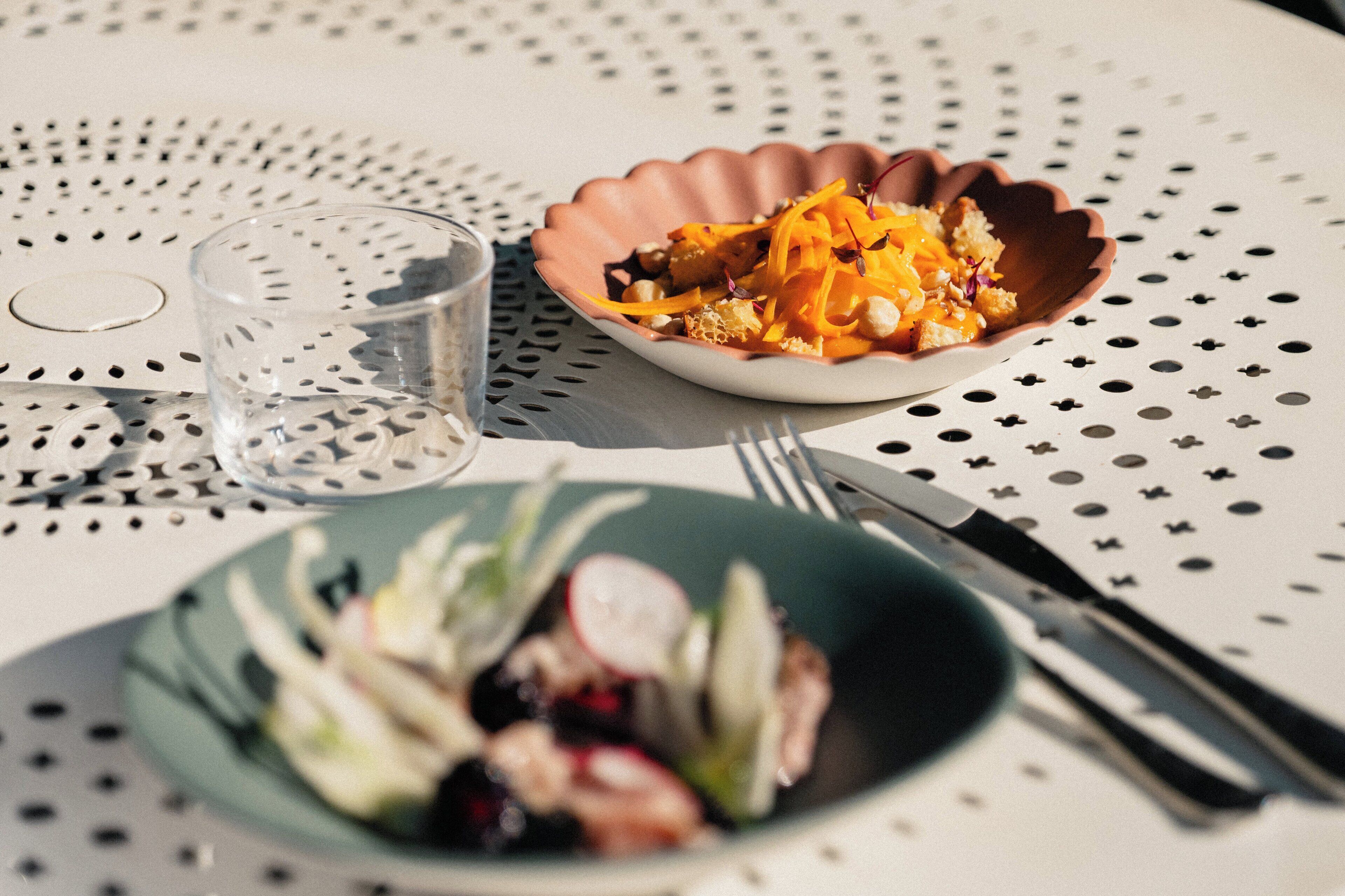 Ett bord med en tallrik med vågformad kant, på vilken det ligger en sallad, och ett glas vatten. På bordet finns också en gaffel och en kniv.
