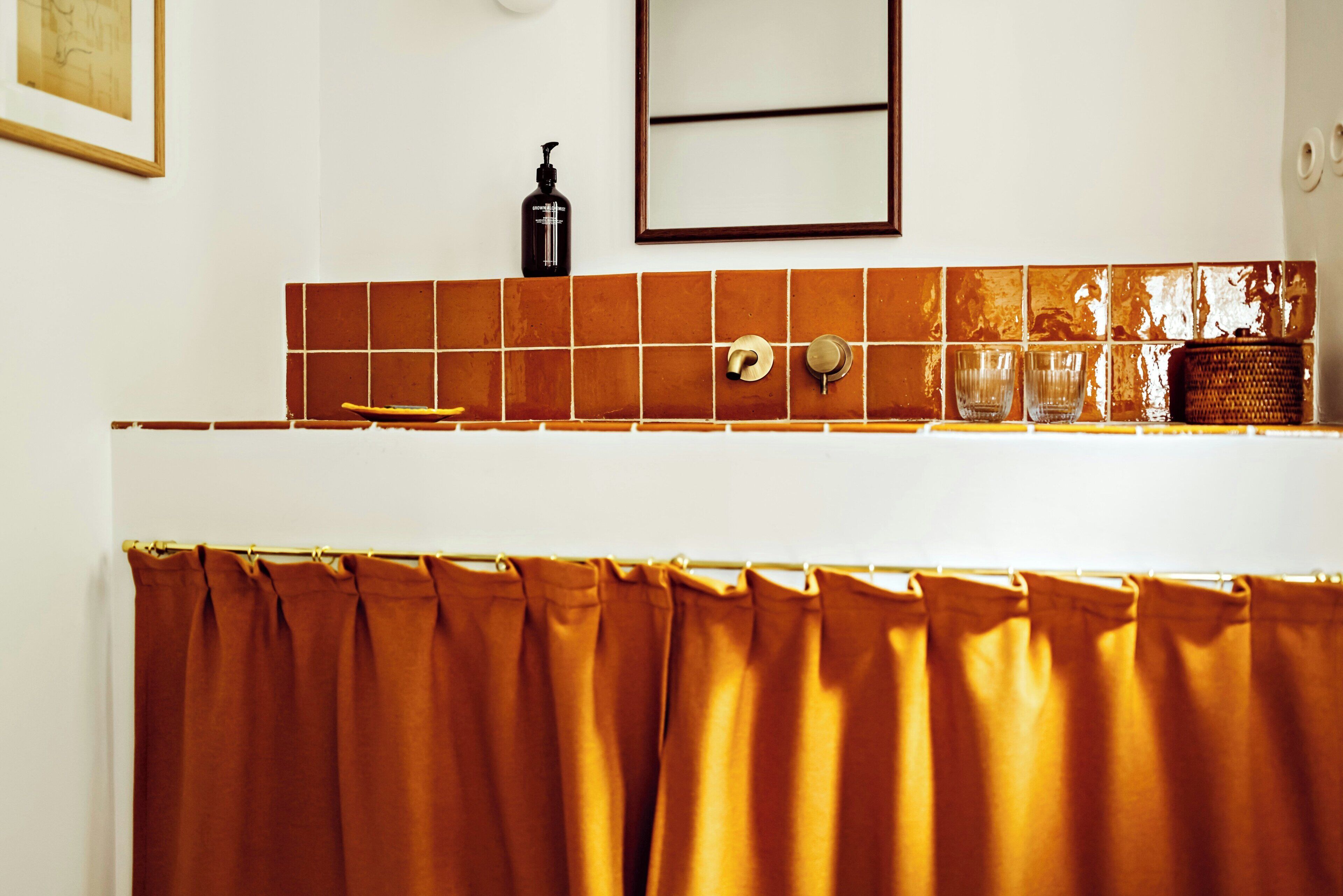 A bathroom with a tiled backsplash, a mirror, a shower curtain, and a soap dispenser.