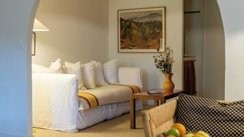 A hotel room with a bed, a sofa, a dining table, and a painting on the wall.