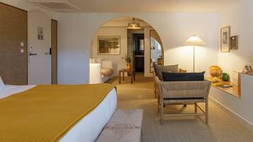A hotel room with a bed, a sitting area with a chair and table, a lamp, and a painting on the wall.