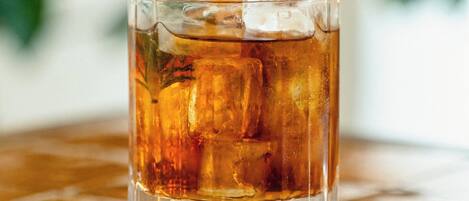 A clear glass with a beverage, ice cubes, and a sprig of rosemary on a reflective surface.