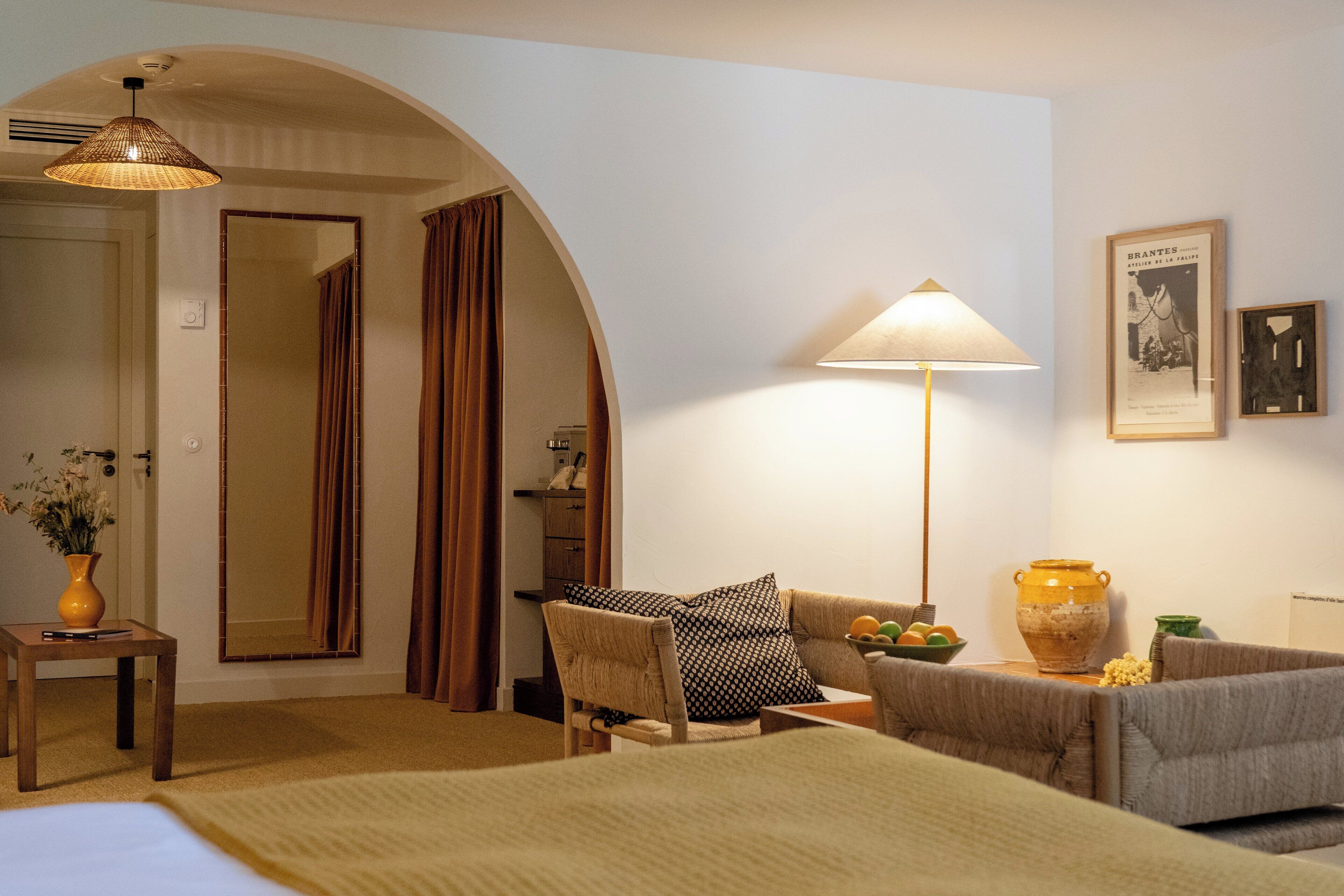 Een hotelkamer met een bed, een bank, een stoel, een lamp, een vaas en een lijst met een afbeelding aan de muur.