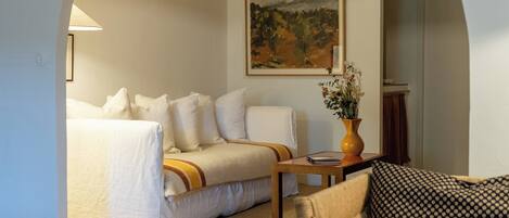 A hotel room with a bed, a sofa, a dining table, and a painting on the wall.
