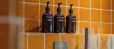 A bathroom with a tiled wall, a hand dryer, and three bottles of 'Grown Alchemist' body wash.