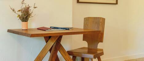 A wooden table with a potted plant and a book, a wooden chair, and a framed picture on the wall.