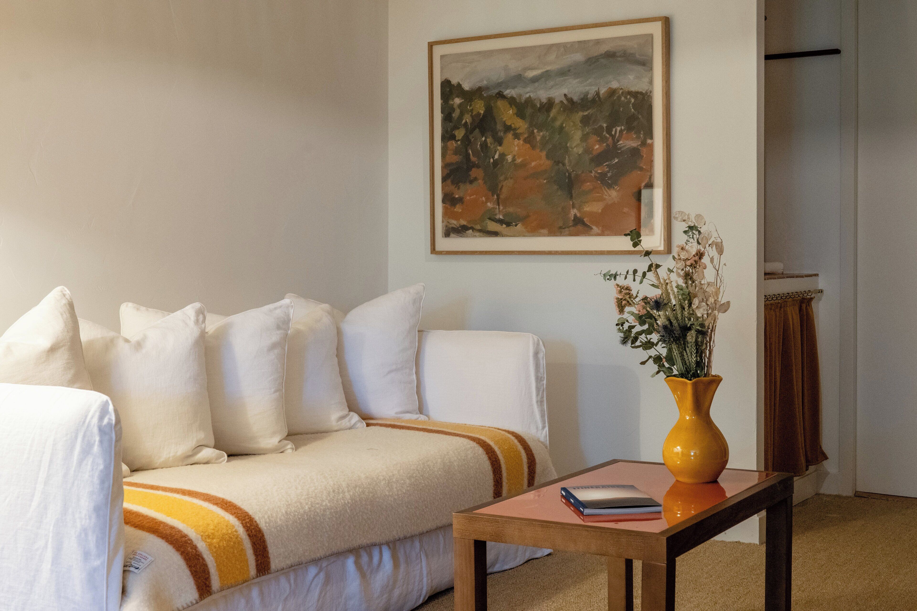Una habitación con sofá, una mesa, un jarrón con flores y un cuadro en la pared.