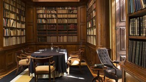 A library with a round table and chairs, surrounded by tall bookshelves filled with books. - Quinta Das Lagrimas (Coimbra)