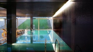 An indoor swimming pool with clear glass walls, a metal ladder, and a view of a green outdoor area. - Quinta Das Lagrimas (Coimbra)