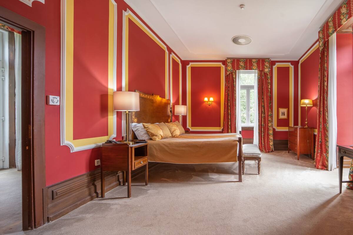 Une chambre d’hôtel avec un grand lit, des tables de chevet, une petite table et une commode.