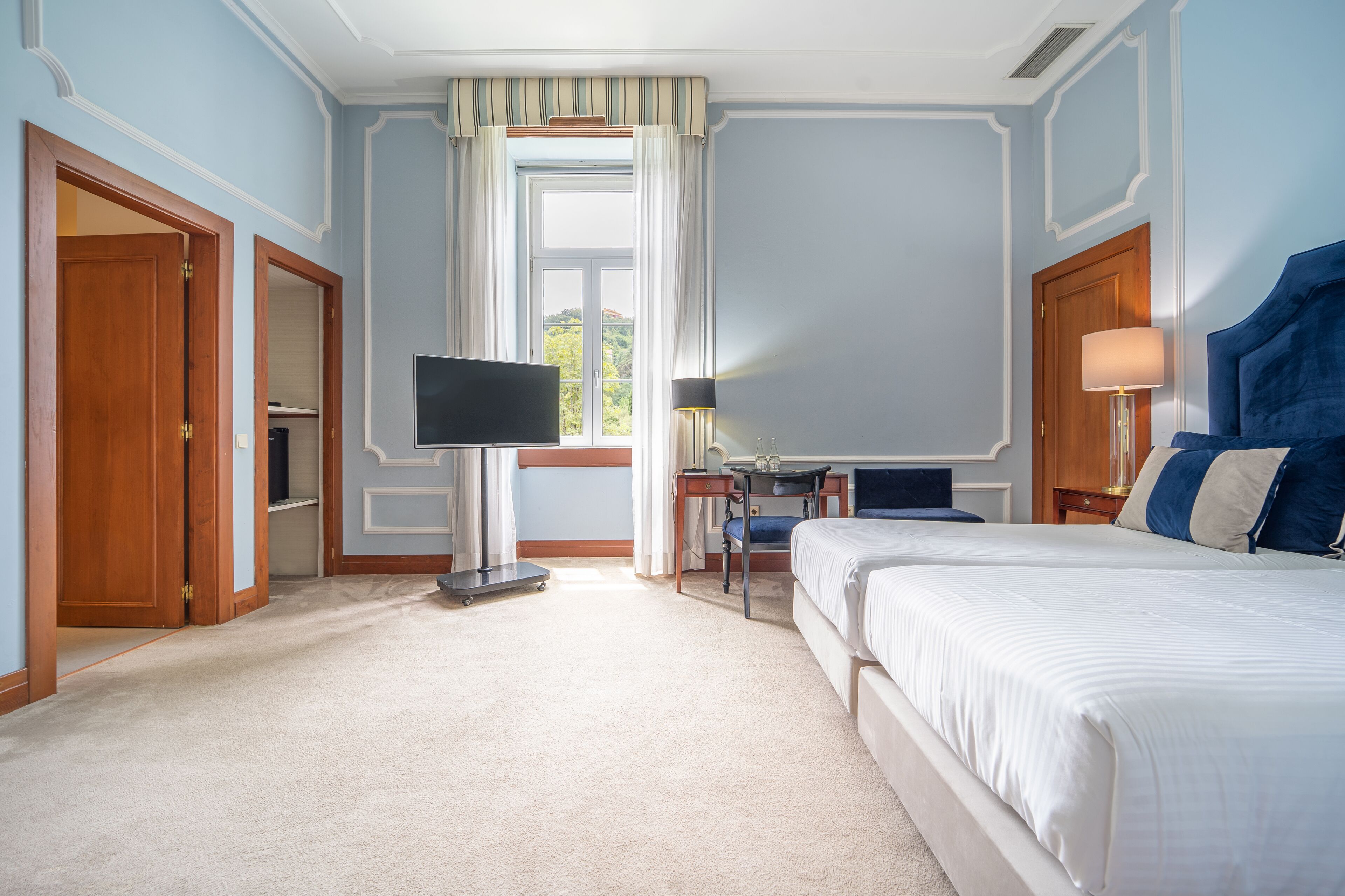 Una habitación de hotel con cama, escritorio, televisión y ventana con cortinas.