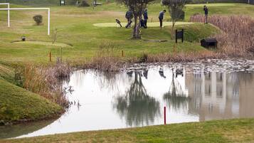 Golfers can enjoy a serene putting experience on the well-maintained grassy area with a pond in the background.