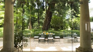 A glass-enclosed outdoor dining area with a table set for four, surrounded by chairs, and framed by columns. - Quinta Das Lagrimas (Coimbra)