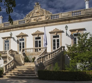 Un edificio imponente con una escalera central, detalles arquitectónicos ornamentales y una bandera.