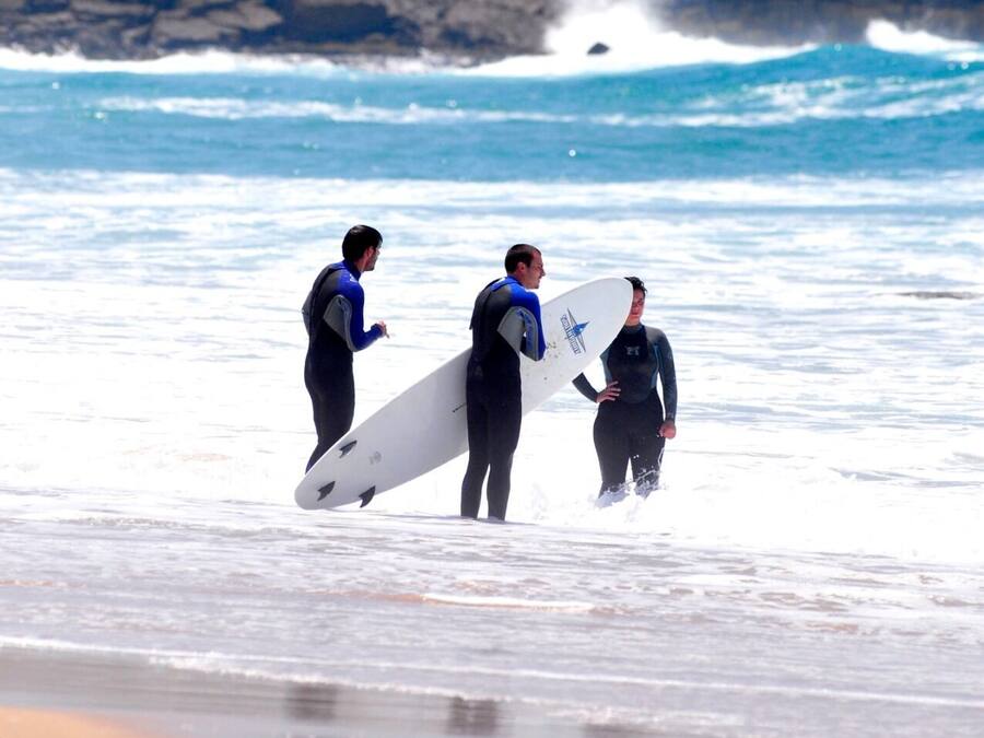 Un edificio con varias banderas en el techo, cerca de una playa donde las olas rompen sobre la orilla.