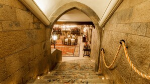 Eine prächtige Treppe mit aufwendigem Teppich und Steinwänden führt zu einem Essbereich mit Tischen und Stühlen.