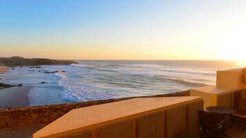 A seaside terrace with a view of the ocean, a stone wall, and a small table and chairs.
