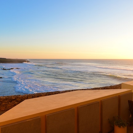 A seaside terrace with a view of the ocean, a stone wall, and a small table and chairs.