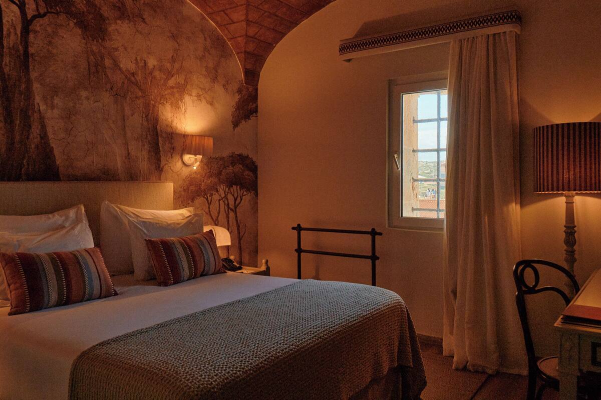 Un dormitorio con una cama grande, una mesita de noche, una lámpara, una ventana con cortinas y techo de madera.