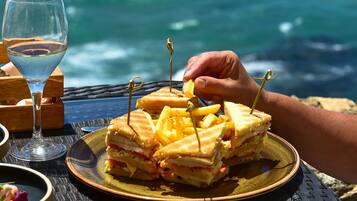 Un sándwich con palillos de dientes sobre un plato, una copa de vino y vista al océano.