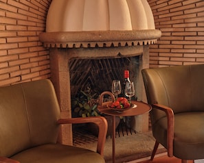 A brick fireplace with a stone mantle, two upholstered chairs, a small round table with a plate of strawberries and two wine glasses.