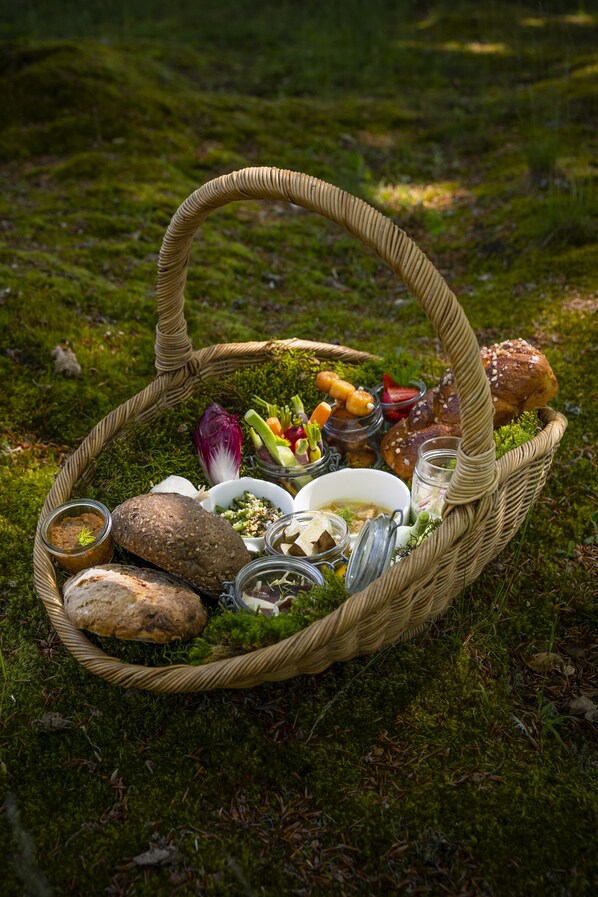 Una cesta de picnic llena de comida y bebidas sobre un suelo cubierto de musgo.
