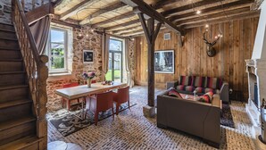 A rustic cabin interior with a stone wall, wooden beams, a dining area, a sofa, and a fireplace.
