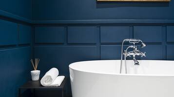 Een moderne badkamer met een vrijstaand bad, een klein tafeltje met een handdoek en rietverspreider, en een lijst met een afbeelding aan de muur.